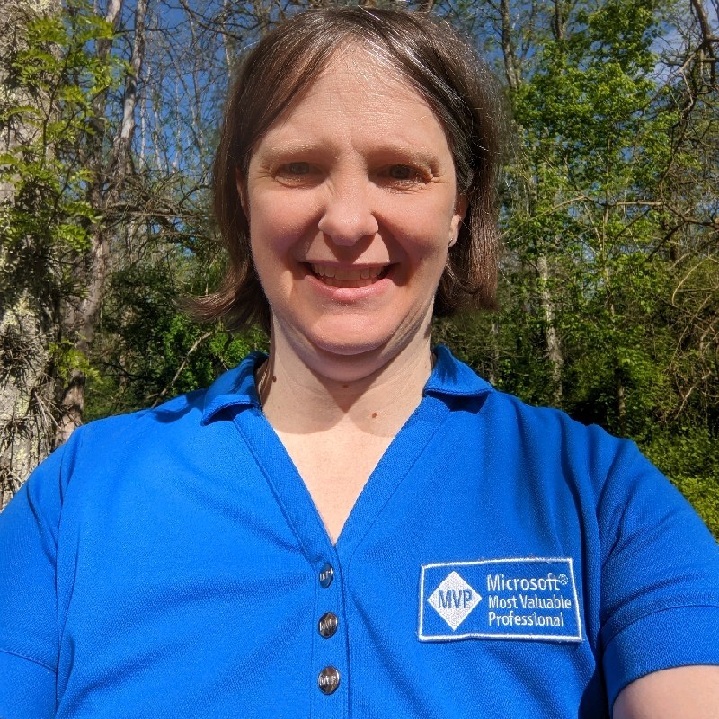 Sadukie, wearing her Microsoft MVP snap polo and smiling while outside at her cabin